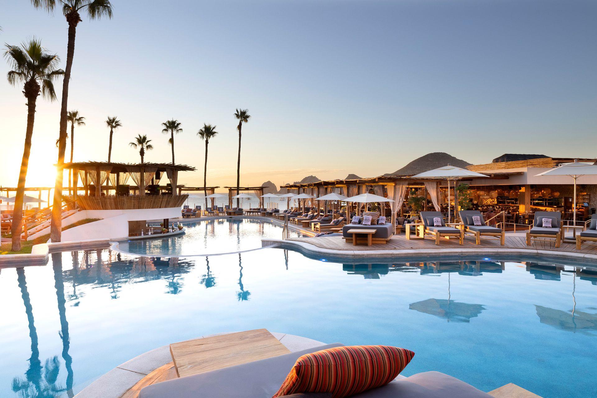 Luxury beachfront resort with pool, palm trees, and lounge chairs at sunset.